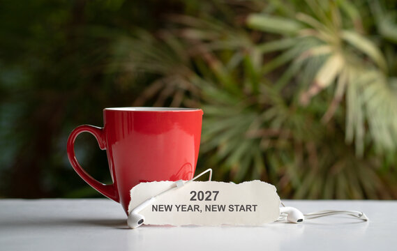 2027 New year new start - message on a piece of paper next to red coffee cup and earphones.