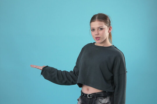 Young Teenage Girl Gesturing and Presenting Copy Space on Blue Background