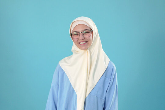 Happy Young Muslim Woman in Glasses and Cream Hijab Smiling Against Blue Background