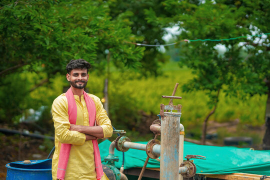 young indian farmer standing with water hand pump at rural village