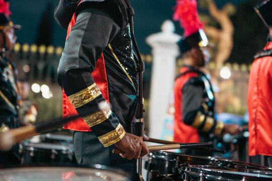 Close up of marching band drummers playing drums in red and black uniforms during a parade at night