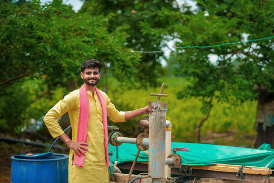 young indian farmer standing with water hand pump at rural village