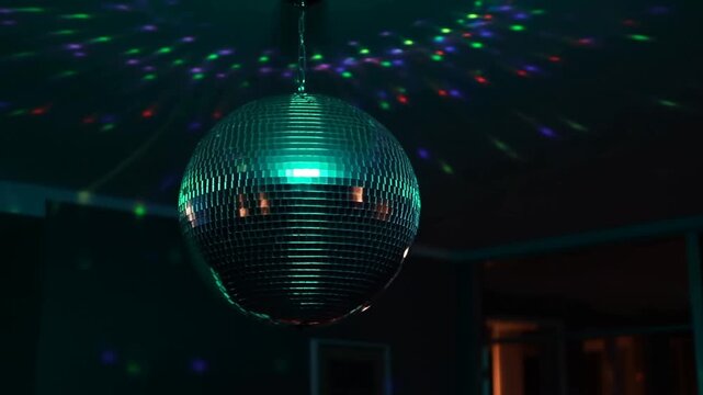 Slow motion tracking shot of disco ball rotating with colored mirror reflections across indoor party room ceiling at night