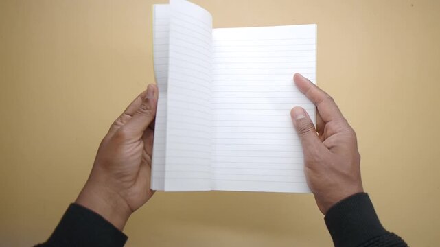Hands hold a blank notebook with lined pages facing the camera