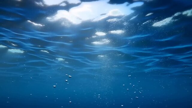 Slow motion tracking shot of bubbles rising beneath ocean surface in open sea with sunlight rays filtering through clear blue water