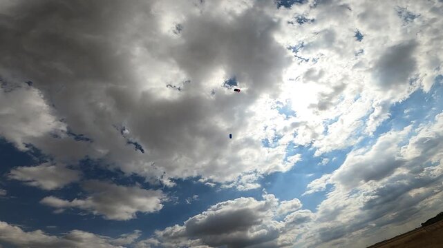Skydivers with wing-type parachutes fly through a beautiful, cloudy sky