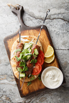 traditional indian minced meat skewers Seekh Kebab with yogurt, naan bread and vegetables closeup on the wooden board. Vertical top view from above