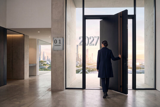 Donna in cappotto blu vista di spalle apre una grande porta in un ingresso moderno in cemento, verso una citt&agrave; futuristica, con il numero 2027 in vetro e un calendario a muro con 01 January.