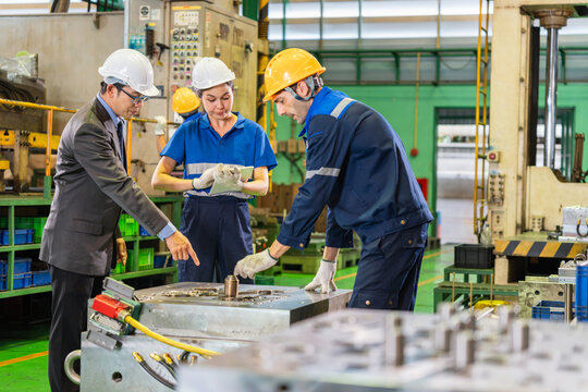 Industrial manager pointing at machinery mold while engineers check specs on digital tablet, Diverse engineering team discussing machinery mold maintenance with factory supervisor