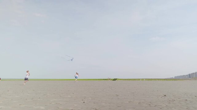 Unrecognizable boy and girl running with colorful kites slow motion on a wide sandy beach and a blue sky camera movement