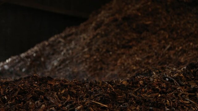 Close-up footage of a large pile of brown shredded wood chips and organic biomass material. The rough texture and layered fragments illustrate organic material processing, biomass resources, wood recy