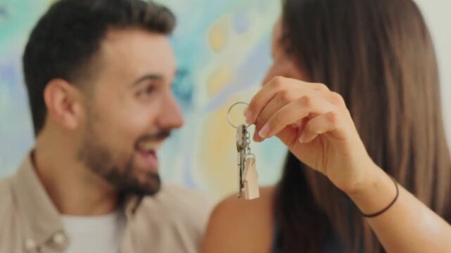 A joyful pair displays a keyring with two keys in a warm living space. The shot emphasizes happiness, new beginnings, and shared achievement, with soft lighting and colorful wall art in the