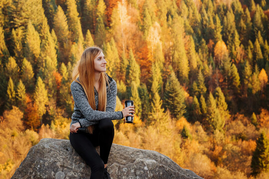 Woman with travel mug enjoys autumn mountain view