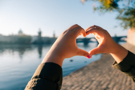 Tourist makes heart shape with hands near river in Prague