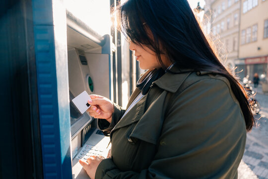Person uses ATM card at cash machine in city street during daytime
