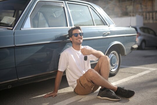 Happy man with sunglasses sits next to his vintage car