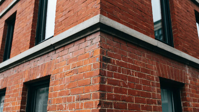 Close-up of a red brick building corner with windows and concrete trim.