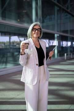 Businesswoman holding coffee cup and folder outside modern building