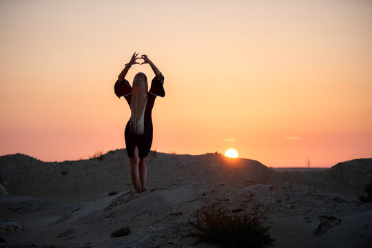 Zikreet, Qatar - April 10, 2026: Silhouette of a woman standing on desert sand dunes with arms outstretched toward a golden sunset. a woman enjoying freedom and serenity during golden hour in a rocky 