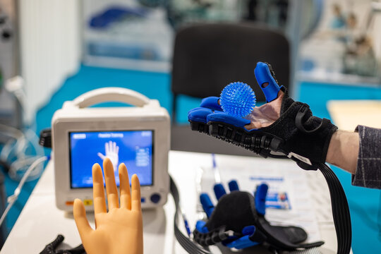 Close up of a robotic rehabilitation glove holding a blue spiky therapy ball during a hand exercise, innovative assistive technology for restoring mobility and motor skills.