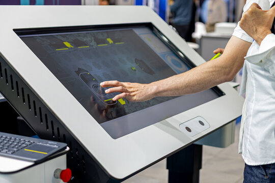 Man interacting with a large industrial touchscreen control panel at a modern technology exhibition, close up of hand operating a digital interface for automation and engineering.