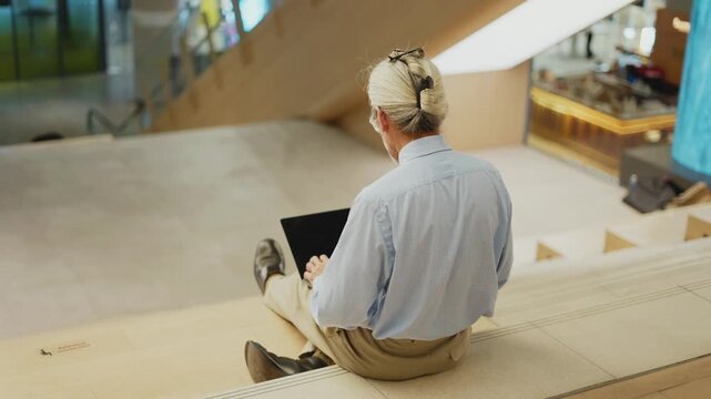 High angle rear view of senior man typing on laptop in mall