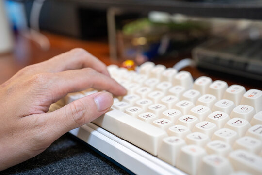 Close-up of a male hand typing on a modern white keyboard with soft lighting.