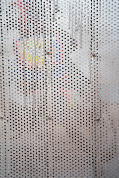Abstract close-up of perforated metal wall with colorful graffiti peeking through.