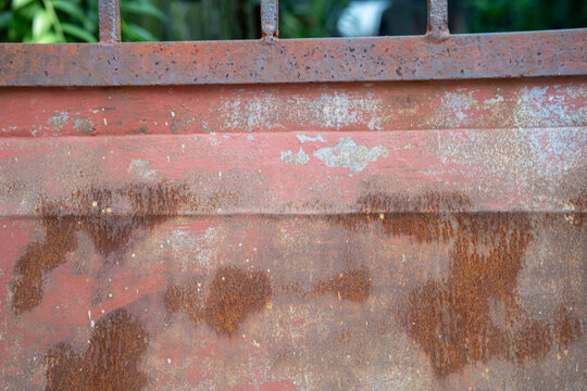 Textured rusty metal panel with weathered red paint and streaks.