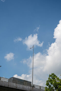 Clear blue sky with fluffy clouds and a streetlight near a highway overpass.