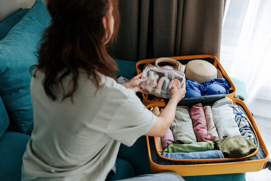 Woman packs yellow suitcase with travel essentials indoors