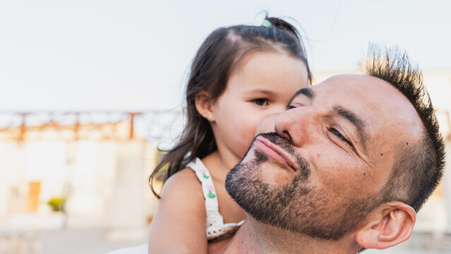 A father carries his daughter outdoors while grimacing