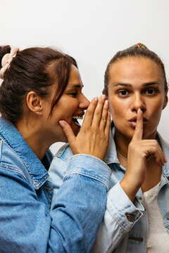 Woman whispers a playful secret to her twin sister demanding silence
