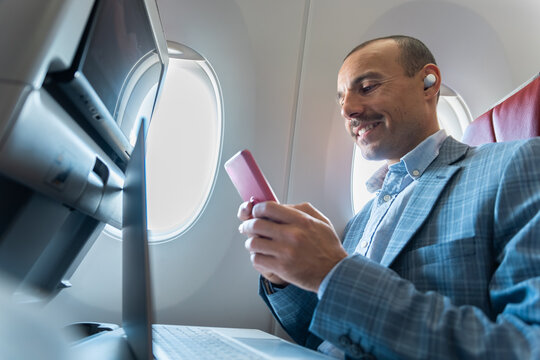 Smiling businessman uses smartphone on an aircraft flight