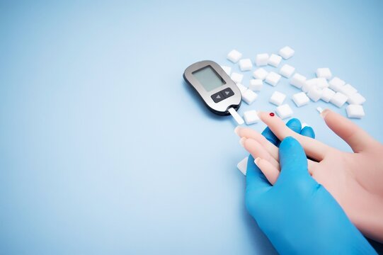 Diabetes concept with blood glucose meter, sugar cubes, blue awareness ribbon and medical gloves on blue background