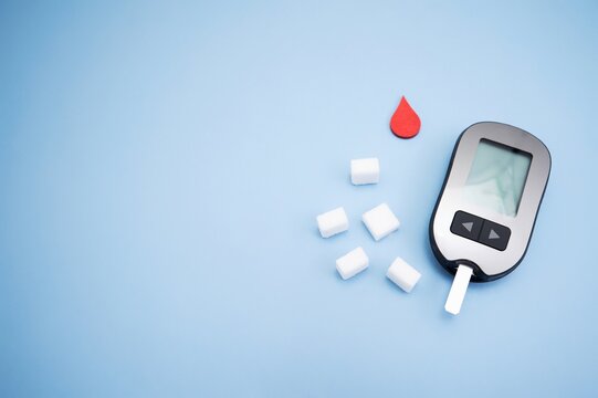 Diabetes concept with blood glucose meter, sugar cubes, blue awareness ribbon and medical gloves on blue background