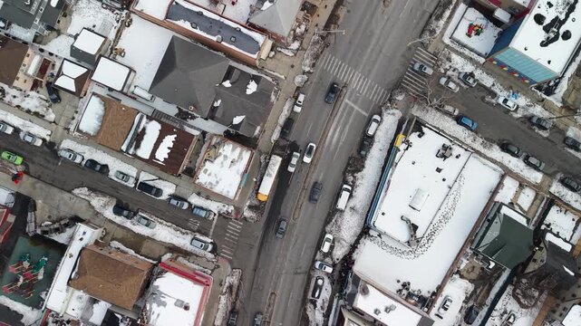 A curved road junction and corner buildings break the pattern of snowy residential blocks in this Queens aerial view, showing rooftops, streets and tree lined blocks.