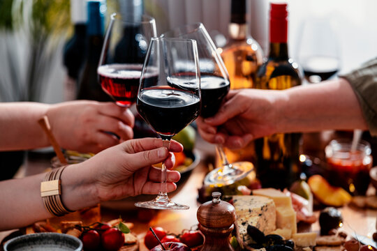 Red wine glasses clinked by friends during autumn lunch in cozy restaurant - group sharing gourmet Merlot tasting experience. Festive celebration and charcuterie food pairing meal.