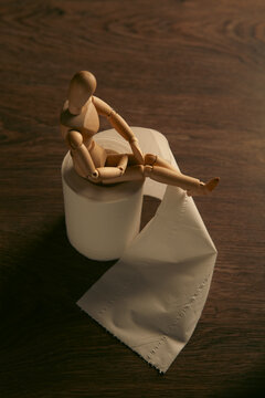 Wooden mannequin with toilet paper on a wooden background.