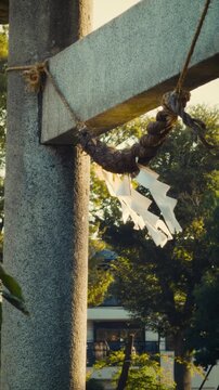 cinematic vertical low angle shot panning left on a traditional japanese stone torii gate with a sacred shimenawa rope and white shide paper streamers blowing in the wind during golden hour sunset
