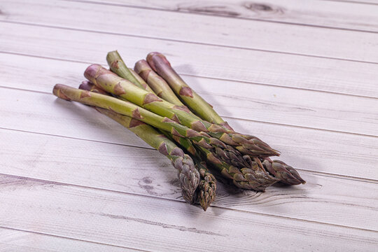 Rustic whitewashed wooden table with fresh green asparagus spears and purple tips arranged diagonally, raw spring vegetables for healthy cooking