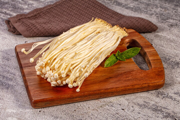 Enoki mushrooms with green basil leaf on wooden cutting board, raw fungus vegetable © Andrei Starostin