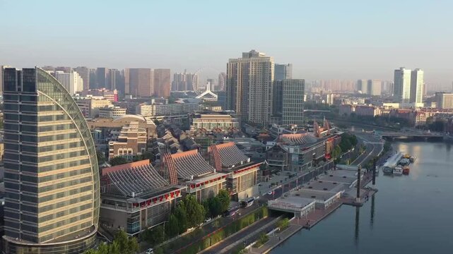 Aerial drone footage of Tianjin Ancient Cultural Street&rsquo;s traditional roofed buildings along the Hai River, juxtaposed with modern skyscrapers and the distant Tianjin Eye Ferris wheel under soft.