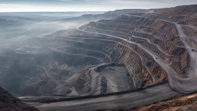 Aerial view of massive open pit mine with winding haul roads and extraction terraces. Industrial mining landscape representing mineral resource production, heavy machinery and environmental impact.