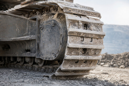 Close-up of tracked excavator undercarriage at a rugged quarry site. Heavy construction machinery for mining, earthmoving, excavation, and industrial infrastructure development.