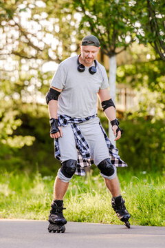 Adult man wearing protective gear rollerblading along paved walkway outdoors in bright daylight