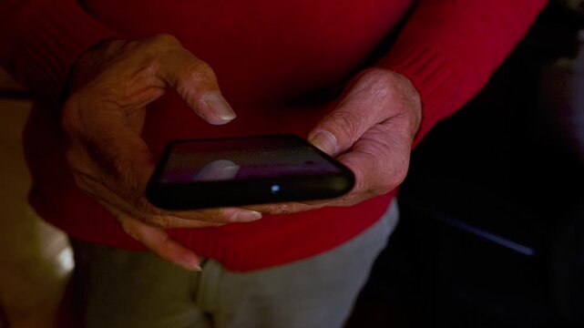Close up of an old Man's wrinkled hands holding and using a mobile phone. He is typing a text message and scrolling on the touchscreen