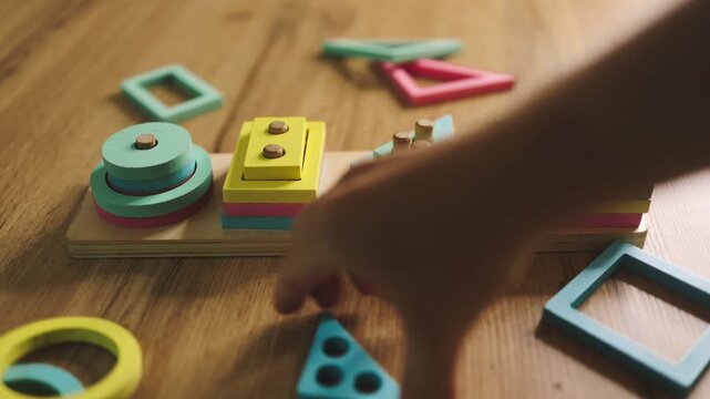 Hands place geometric shapes into a wooden shape sorter, demonstrating a hands-on activity for shape recognition and fine motor practice.

