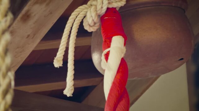 cinematic horizontal low angle close-up shot panning right on a traditional japanese shinto shrine bronze bell and red and white braided rope hanging under wooden eaves