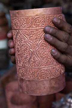 Hands holding an engraved copper cylinder with floral patterns, Jammu and Kashmir, Srinagar, India